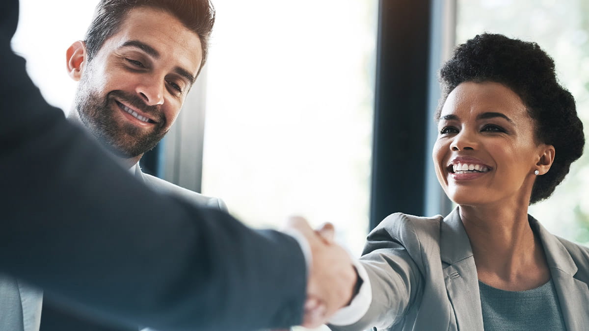 A professional woman smiling while shaking hands with a business partner during a successful meeting.