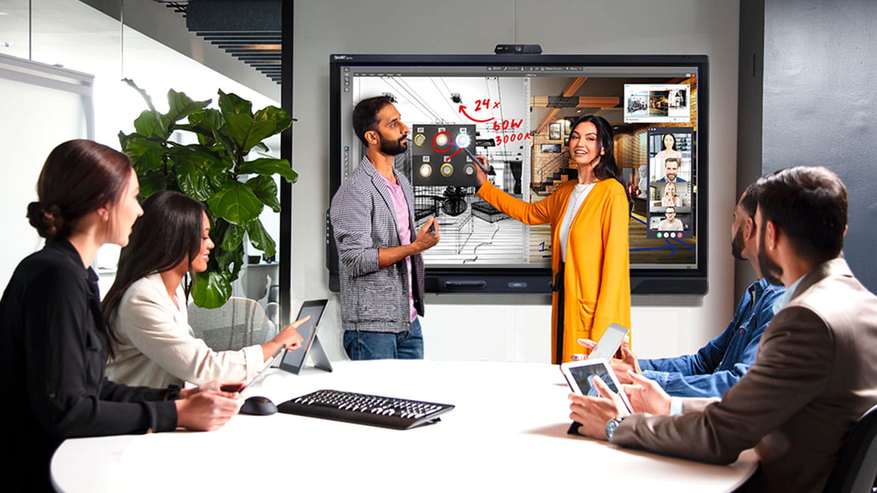 Professional team collaborating using a SMART board in a modern office setting. The interactive display shows complex diagrams and video conferencing tools, enhancing the group's productivity.