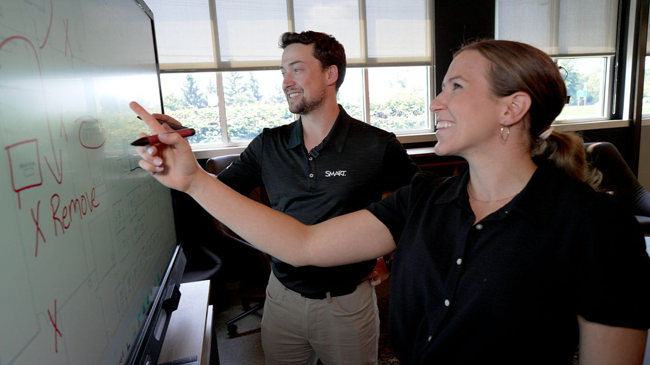 A product demo in progress with two colleagues interacting on a SMART Board to demonstrate features.